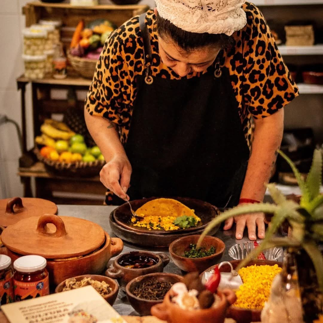 Chef Aline Rocha finalizando um prato na cozinha, cercada de panelas de barro
